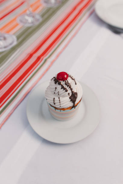 Chopped view of a cupcake with a cherry on the top on a plate served on a long table.