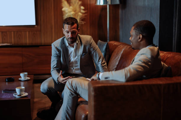 istock Two businessmen having a conversation on a leather couch in a hotel lobby 2199672544
