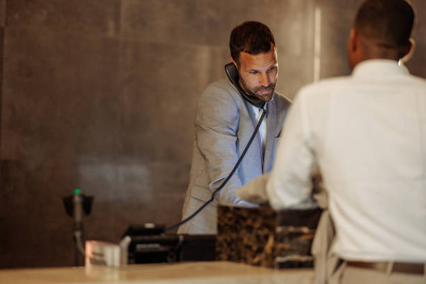 Businessman engaging in a phone conversation while completing the check-in process at the hotel reception desk, showcasing modern hospitality