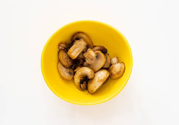 Sautéed champignon mushrooms served in a small yellow bowl against a white background.