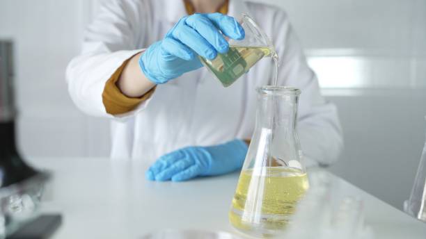 istock A scientist, wearing a lab coat and blue protective gloves, is pouring a yellow liquid from one beaker to another in laboratory, close up. Medicine and science concepts 2199679615