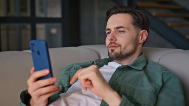 istock Chilling brunette looking cellphone lying beige sofa closeup. Man taking break 2199683619