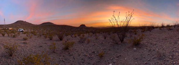 Silhouetted ocotillo cactus reach for a beautiful sunset, as a travel camper van and mountain bike remain parked at a broken down windmill in the Chihuahuan Desert of Big Bend Ranch State Park in west Texas.
