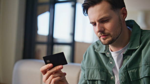 istock Man holding credit card making purchase home closeup. Guy doing online payment 2199688353