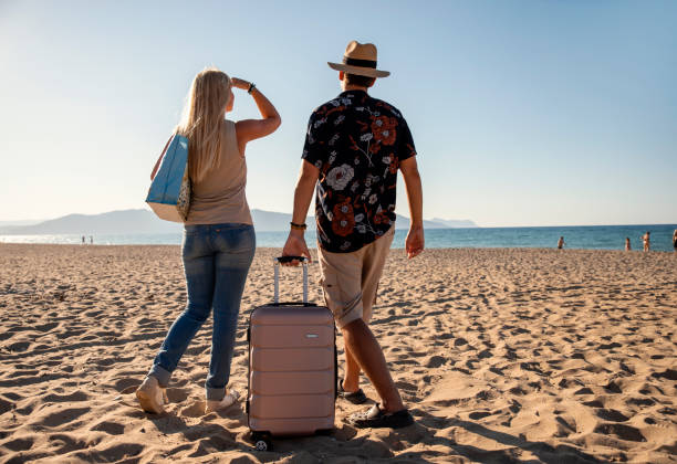 istock Rear view of couple with suitcase on a beach getaway 2199690294