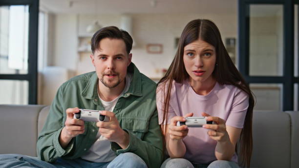 istock Focused friends playing video games using controllers sitting couch together 2199693935