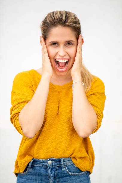 Close-up portrait of cheerful young woman with surprised expression holding her face against white background