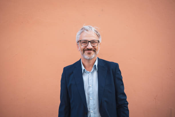 istock Confident mature man in glasses standing against peach background 2199700728