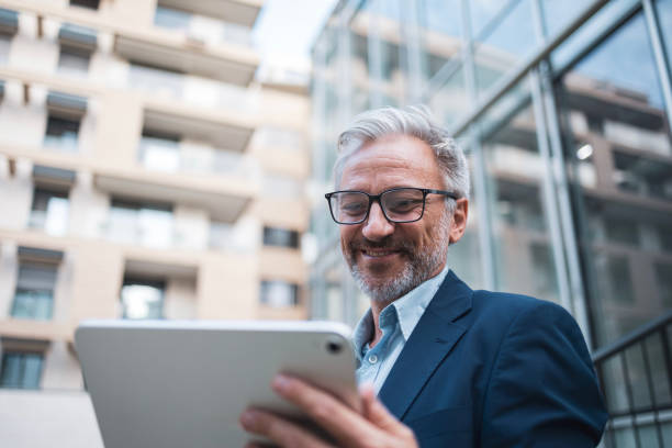 istock Smiling businessman using tablet outside modern office building 2199700746