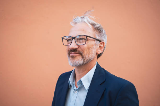 istock Confident mature man in glasses smiling against a peach color wall 2199700749