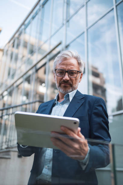 istock Mature businessman using tablet outside modern building 2199700750
