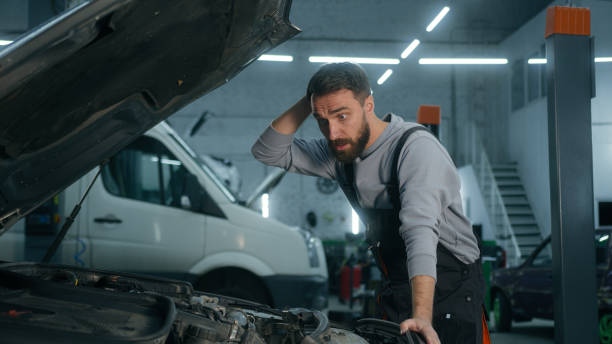istock Caucasian man professional auto mechanic technician car service worker opening automobile hood looking under bonnet shocked male confused problem vehicle breakdown broken transport in garage station 2199702450
