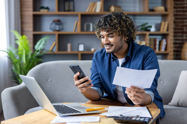 istock Happy man using smartphone and laptop for online bill payment at home 2199715277