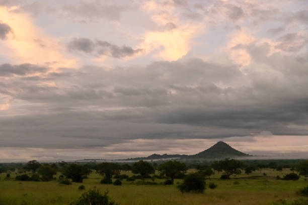 A tranquil scene unfolds with a lone mountain rising above a lush expanse under a dramatic sky, highlighting Tanzania's diverse natural beauty.