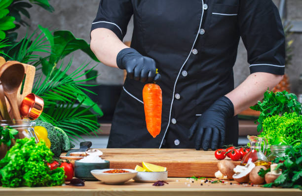 istock Chef holds big organic carrot in hands. Cozy kitchen with wooden table, kitchenware, vegetables, herbs and ingredients for cooking. Healthy vegan eating, culinary, recipes, food blogging comcept 2199754470