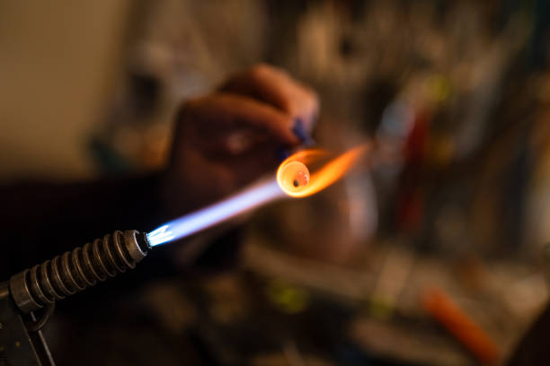 A woman making small products in a glass workshop by melting glass rods in a flame.