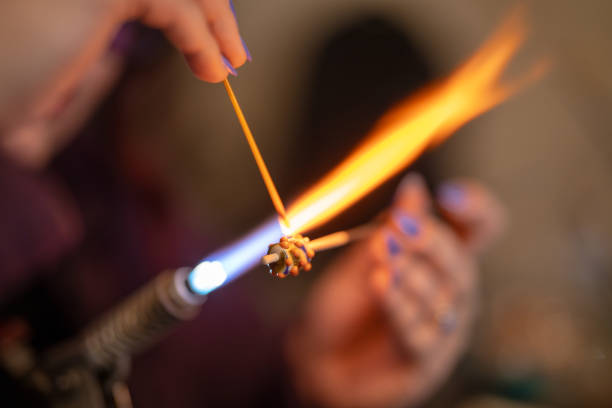 A woman making small products in a glass workshop by melting glass rods in a flame.