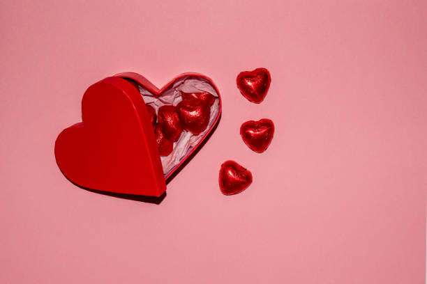 istock Red heart-shaped box filled with chocolates and scattered mini hearts on a pink background during Valentine's celebration 2199773224