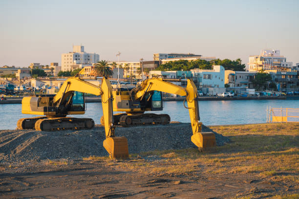 yellow excavators lined up at a construction site near a waterfront, bathed in warm sunlight. The industrial landscape highlights the progress of urban development and infrastructure at enoshima kamakura beach