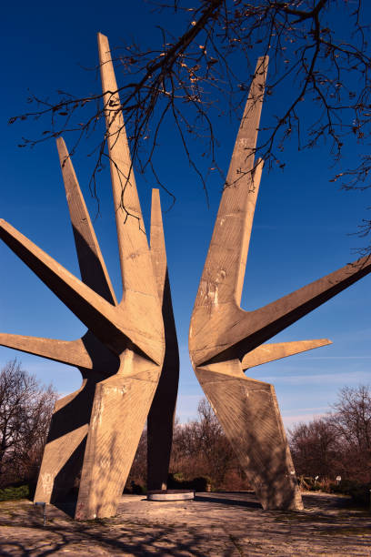 The striking WWII monument on Kosmaj Mountain, Serbia, features a brutalist concrete design symbolizing resistance and freedom. The structure stands tall against a deep blue sky at sunset.