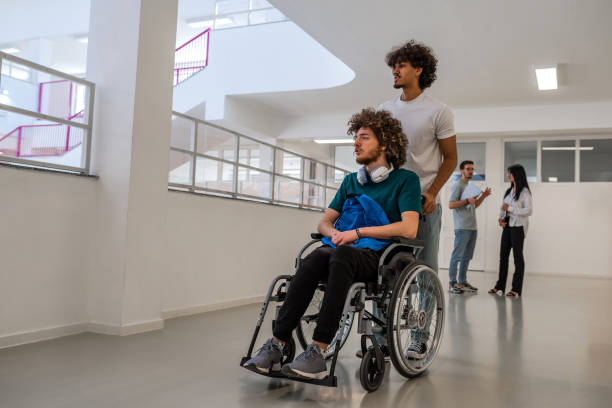 istock Group of diverse college students in university hallway, a classmate pushing a friend in a wheelchair as they walk down the school corridor or caregiver walks with a patient through hospital corridor. 2199786678