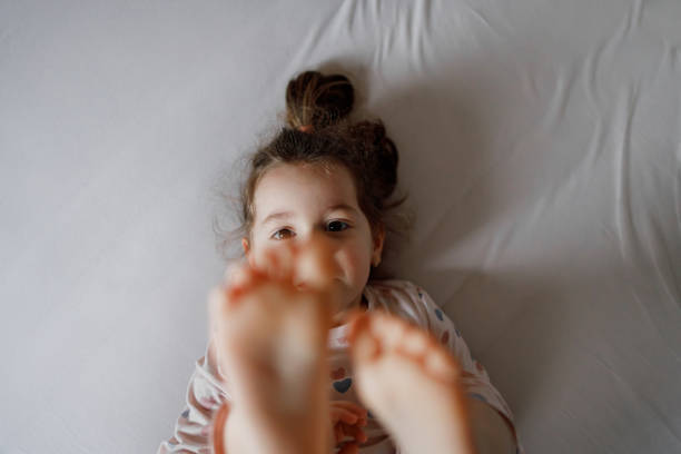A Little Girl in Pajama is laying in Bed with raised legs.