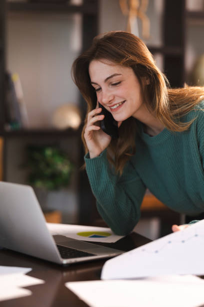 istock Young woman working at home office using laptop and talking on a smartphone 2199800434