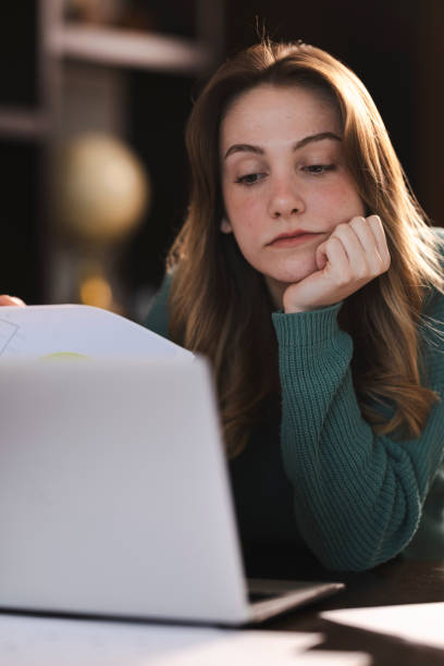 istock Young woman looking bored while working or studying from home, lying on the desk and looking at her laptop 2199800627
