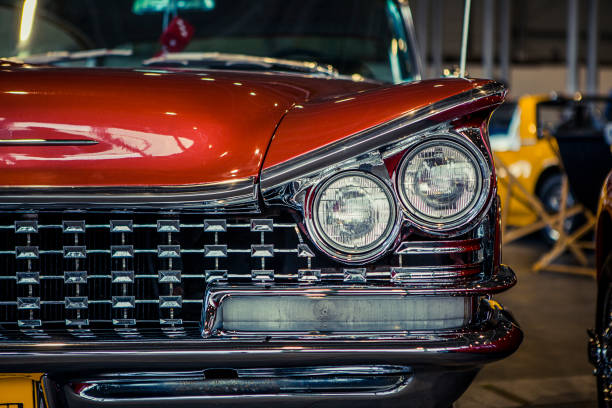 A detailed close-up of a vintage car's rear light and shiny chrome bumper. The sleek lines and polished finish of the car reflect its classic design and well-maintained condition, with a hint of green grass in the background.