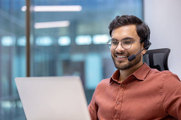 Smiling businessman wearing a headset working on a laptop in an office setting
