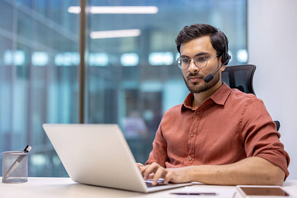 istock Confident hispanic businessman immersed in work on laptop with headset in modern office environment, promoting productivity and communication skills in professional setting 2199803508