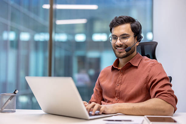 istock Smiling professional man with headset working on laptop in modern office environment 2199803509