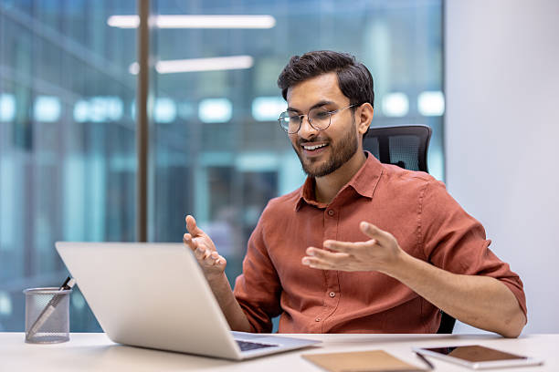 istock Young Hispanic businessman engaging in an online video call from a modern office setting with a laptop 2199803575