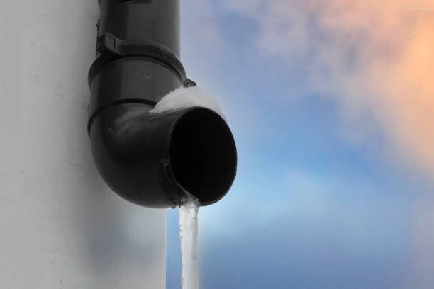 Drainpipe with a frozen stream of water against the sky, a large icicle.