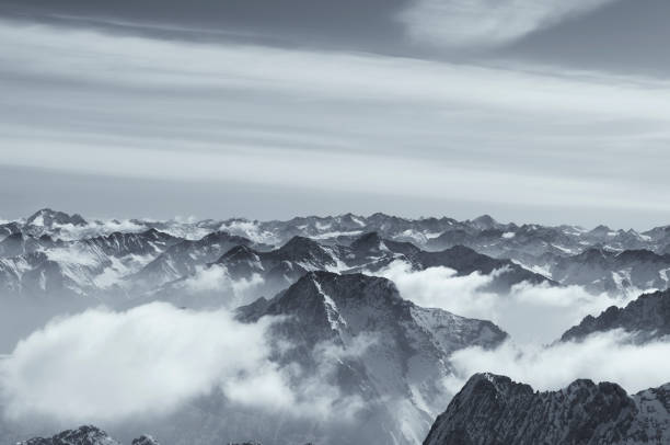 A black and white panoramic view of the snow capped Wetterstein mountains covered by clouds from on top zugspitze in Garmisch-Partenkirchen Germany.