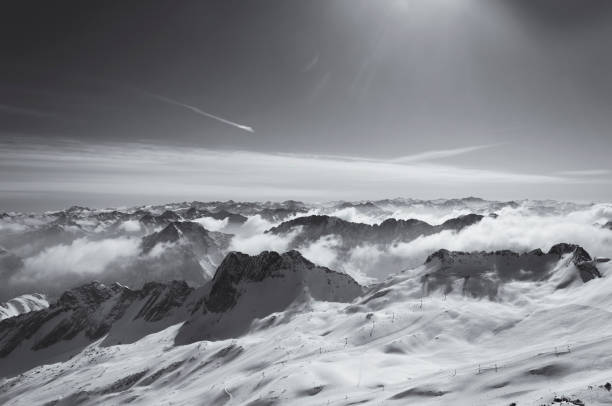 A black and white panoramic view of the snow capped Wetterstein mountains covered by clouds from on top zugspitze in Garmisch-Partenkirchen Germany.