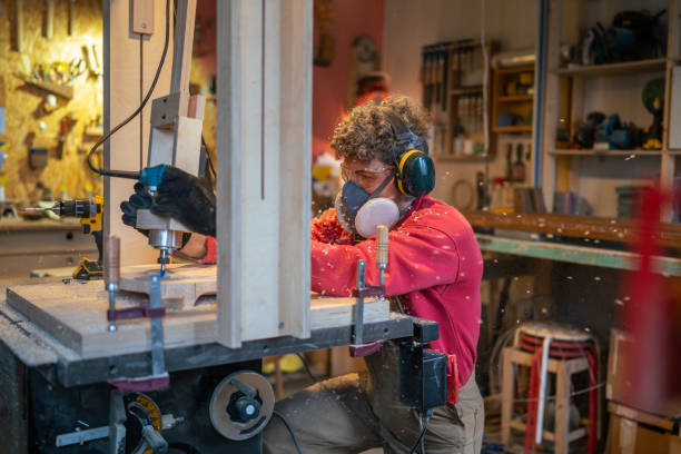 istock Carpentry workshop craftsman master working. Manual wood milling guy holds tool controlling process 2199812635