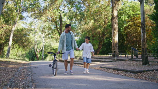 istock Man boy walking sunshine path with bicycle. Positive family talking during walk 2199820048