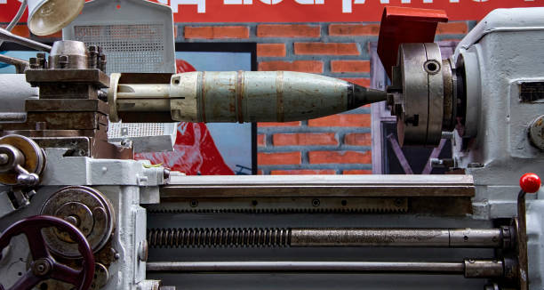 A powerful metalworking lathe is used to shape a large missile, its smooth surface gleaming under the workshop lights. The machine's intricate gears and levers are in motion, carefully guiding the tool as it spins against the metal. The workshop's brick walls add a touch of industrial character to the scene, emphasizing the raw power of the machinery.