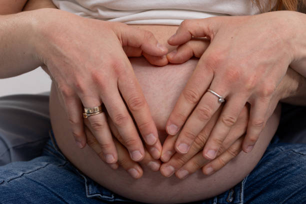 A couples hands form a heart on their pregnant belly, joyfully celebrating love and the anticipation of new life