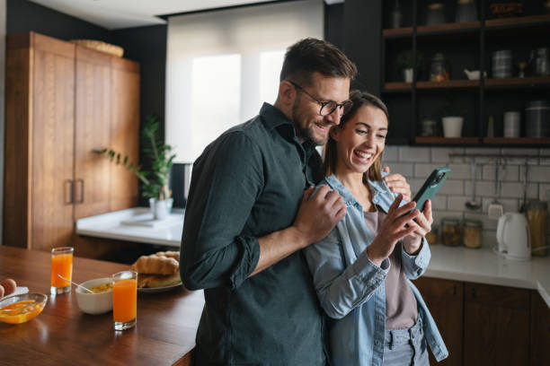 istock Happy couple using smartphone and smiling in kitchen during breakfast 2199831514