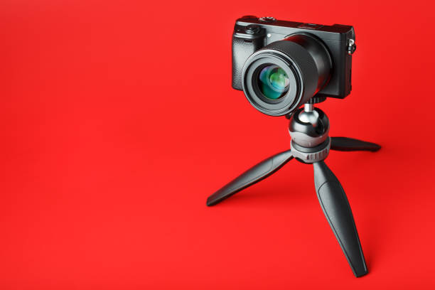 Photo video camera with a tripod, on a red background. For professional video shooting and photography for your blog, reportage. Free space, isolated