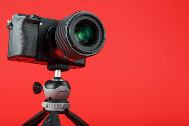 Photo video camera with a tripod, on a red background. For professional video shooting and photography for your blog, reportage. Free space, isolated