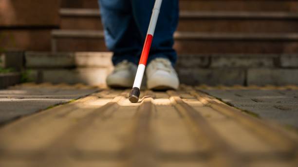 istock A blind woman walks outdoors using a cane along a tactile yellow tile. 2199836688