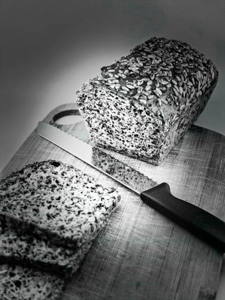 Photo showing freshly baked bread on a wooden board, partially sliced, with a knife lying nearby.