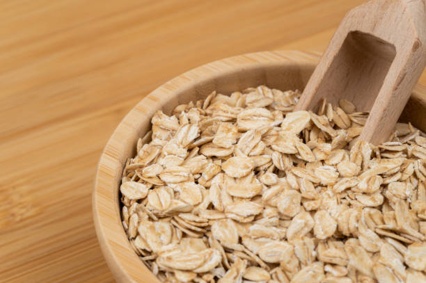 A wooden bowl filled with rolled oats, accompanied by a wooden scoop. The natural texture and golden hues of the oats highlight their organic and nutritious qualities.