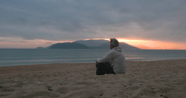 Mature man watches sunrise over mountains from beach, islands and mountains distant, Nha Trang