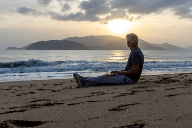 istock Mature uses laptop on beach at sunrise 2199864293