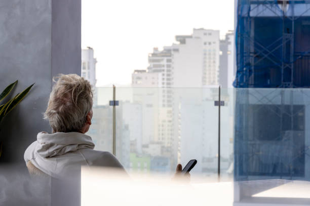 Mature man uses mobile phone rooftop terrace above city