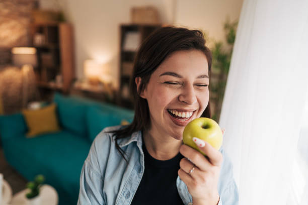 istock Young woman laughing while eating green apple at home 2199870743